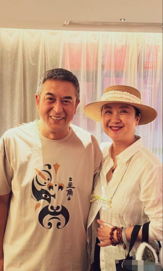 张嘉益微微侧身贴近身旁女士，露出舒展开怀的笑容，神态憨厚。
身边女士目光柔和温润