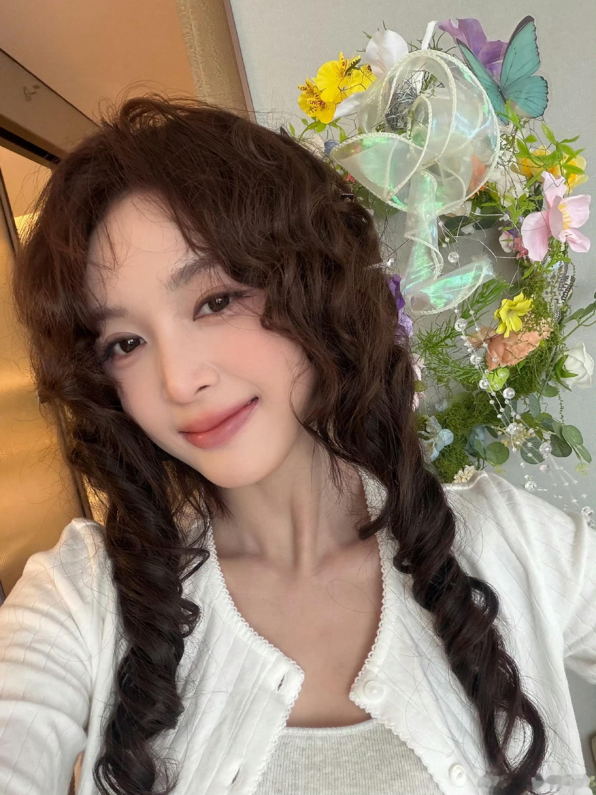 谁能拒绝甜妹吴宣仪！双麻花卷发配上蝴蝶鲜花布景，柔光衬得脸蛋软乎乎的，笑容干净又