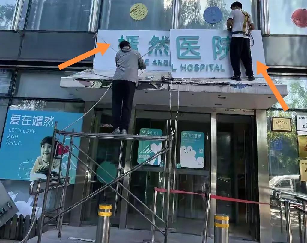 北京嫣然医院两个工人换上新招牌。