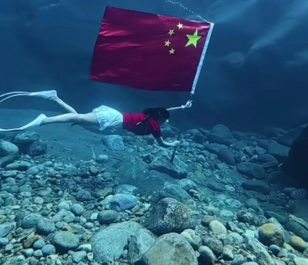 一女生双手握国旗杆在水中游泳，五星红旗随波飘扬（让五星红旗飘扬在五湖四海）。