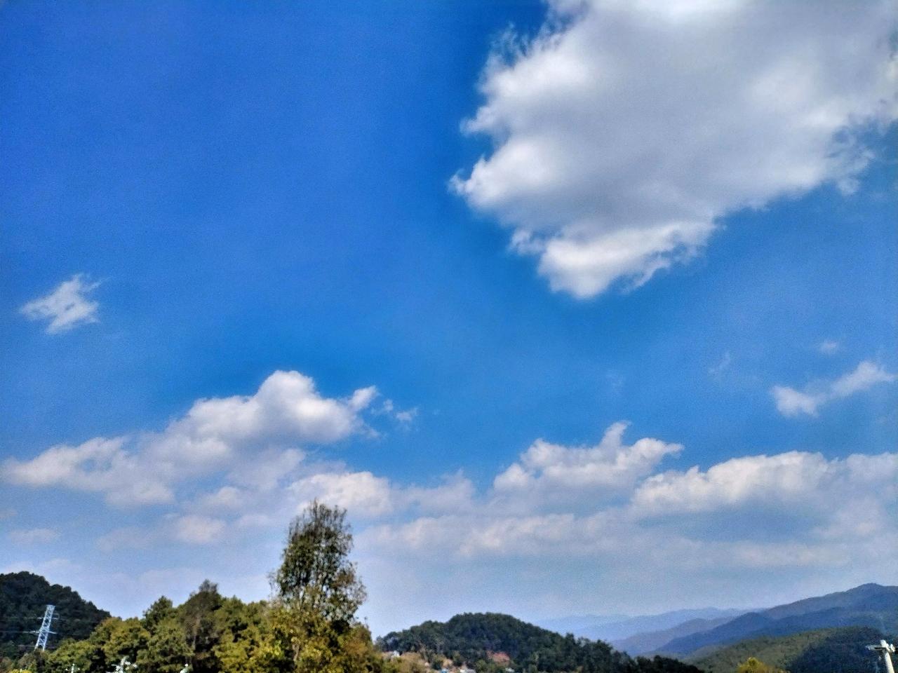 蓝天白云下的静谧山丘，大自然的宁静之美。立于山丘之下，微风轻柔地抚过脸颊，携着山