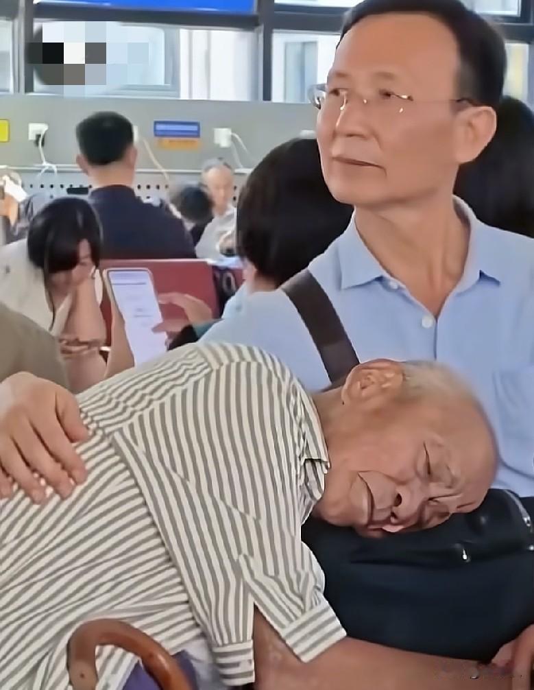 7月21日，北京一候车厅内，一位老父亲依偎着儿子休息，儿子的手臂轻轻地护着儿子的
