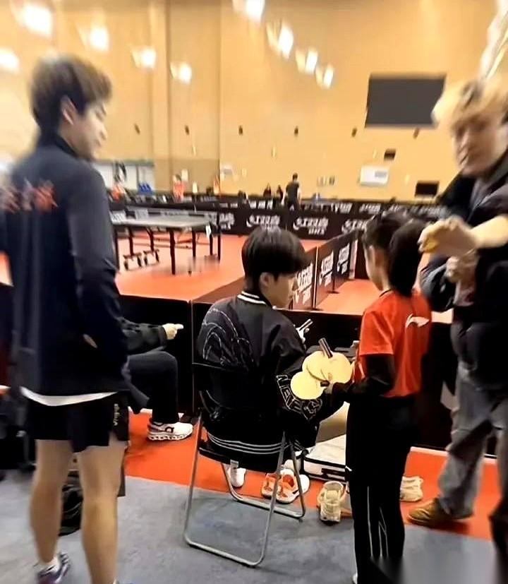 那一摞球拍，比那小女孩的个头都快高了。
就这么直愣愣地递到刚下训、一身是伤的王楚