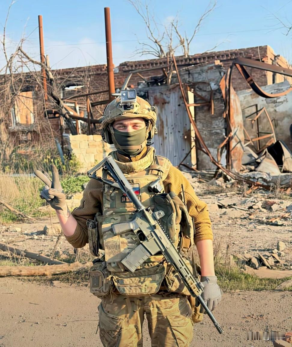 一名俄军士兵身着全地形迷彩装备，在废墟中比出胜利手势。更引人注目的是，他手中并非