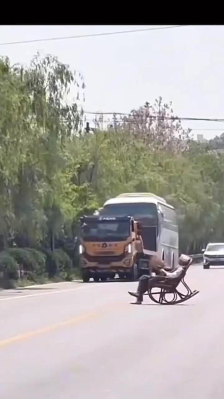 近日，咸阳秦都区马庄街道，一大爷将躺椅摆到马路中间， 翘着二郎腿摇扇子 晒太阳，