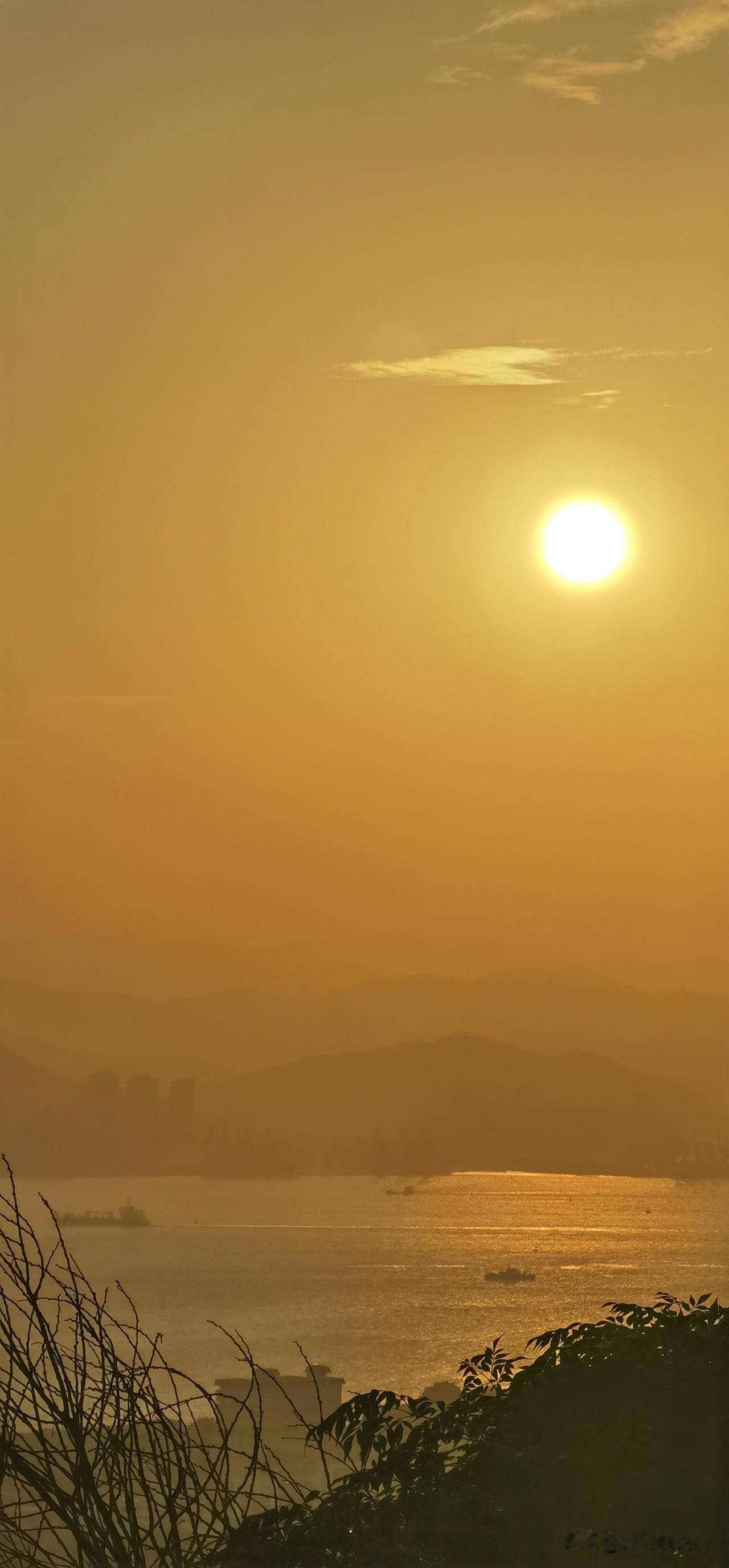 夕阳西下，海面波光粼粼，城市天际线若隐若现，静谧而美丽。