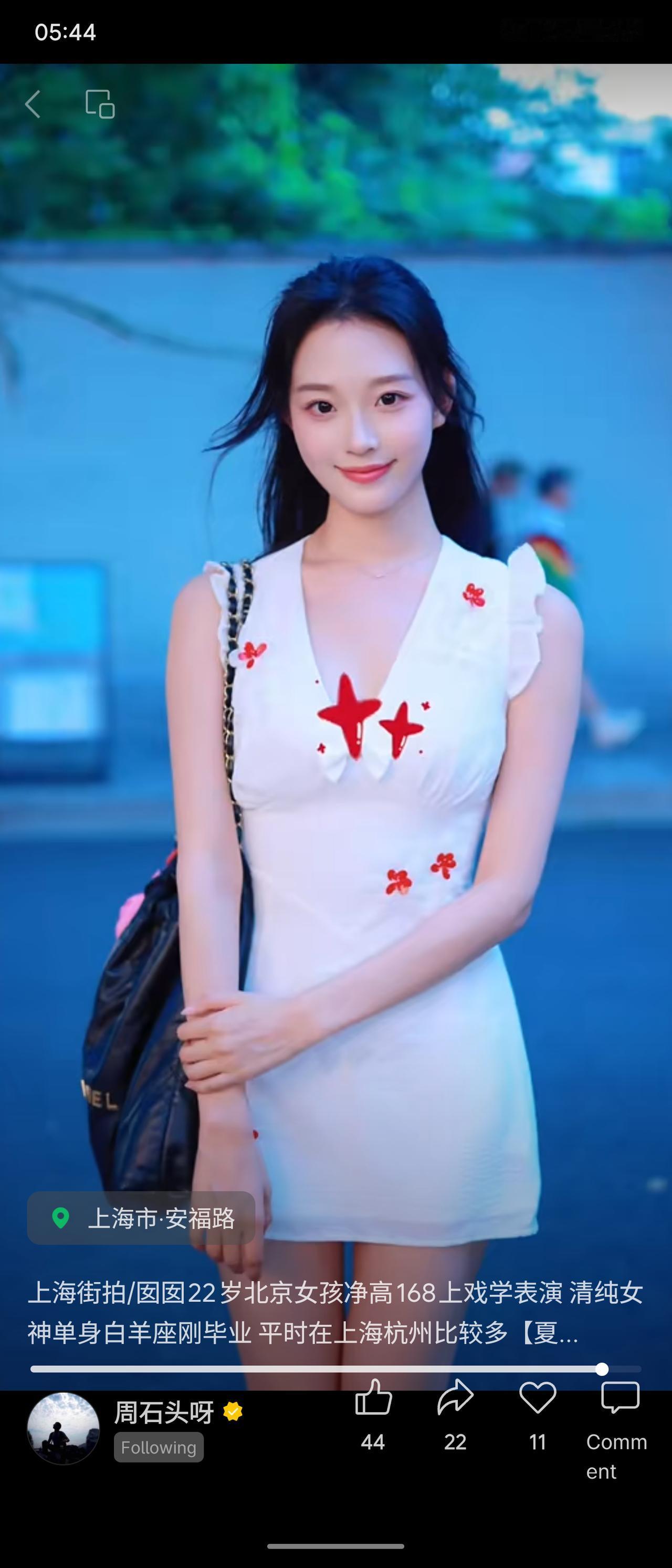 暮色浸染上海安福路，长发女孩身着点缀红色碎花的白款小飞袖短裙。眉眼温婉柔和，笑意