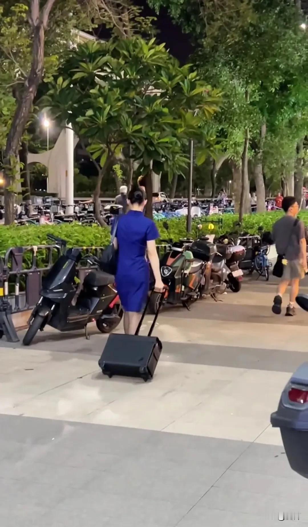 暮色漫染的街头，深蓝色制服裹着挺拔身姿。拉杆箱滚轮碾过夜色，晚风掀动裙摆，每一步