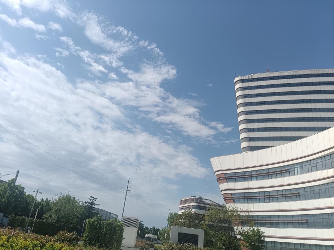 澄澈蓝天缀着柔云，现代建筑线条利落，衬着葱茏绿意，尽显清新明朗。