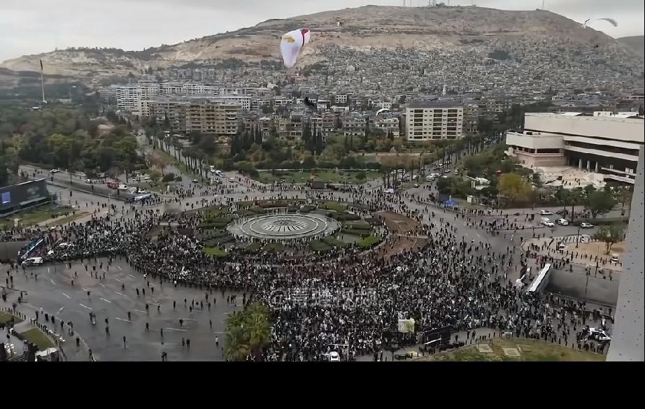 叙利亚群众庆祝阿萨德下台一周年，观看滑翔伞表演。