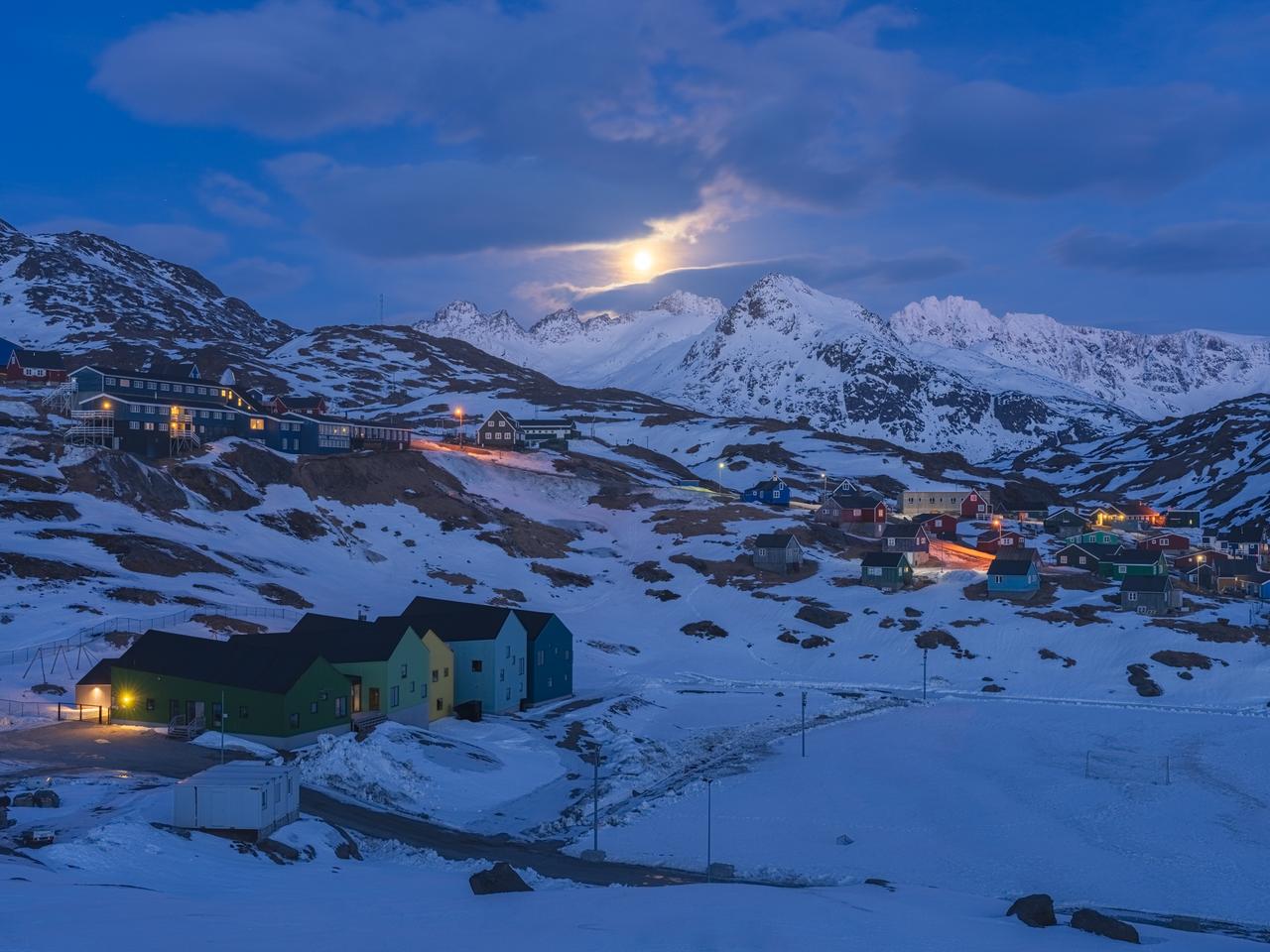 月升时分的格陵兰岛东部塔西拉克镇，金黄色的小镇灯光与皎洁月光交相辉映，背后是被月