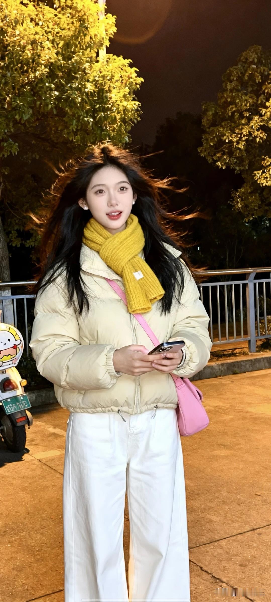 黑色长发  浅米色羽绒服，白色阔腿裤，黄色围巾，粉色挎包，手持手机，夜晚户外场景