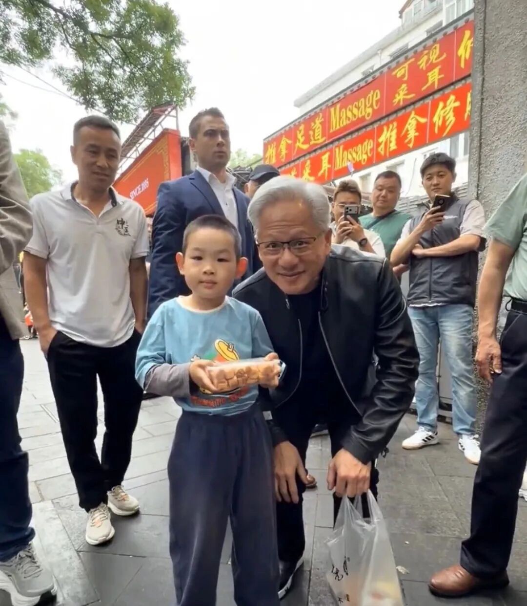 黄仁勋在街边小摊：拿着一串烧烤边吃边笑，喝着奶茶发出满足表情。看到路人举机，就礼