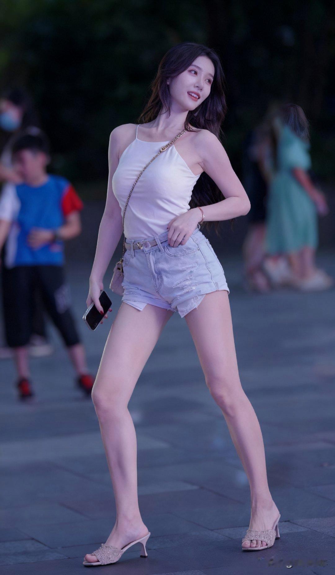 夏日夜晚的街头，轻盈步伐，白色背心与牛仔短裤的完美搭配，尽显青春活力！🌟✨