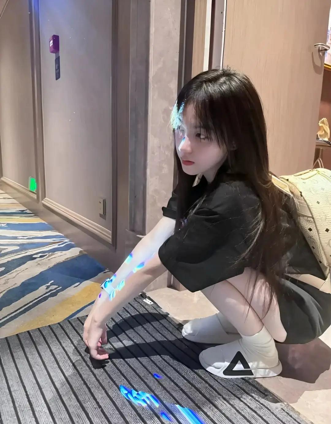 走廊的光影里揉进细碎的蓝，黑T恤裹着随性的松弛感，蹲下来的瞬间，像是和光影玩了一