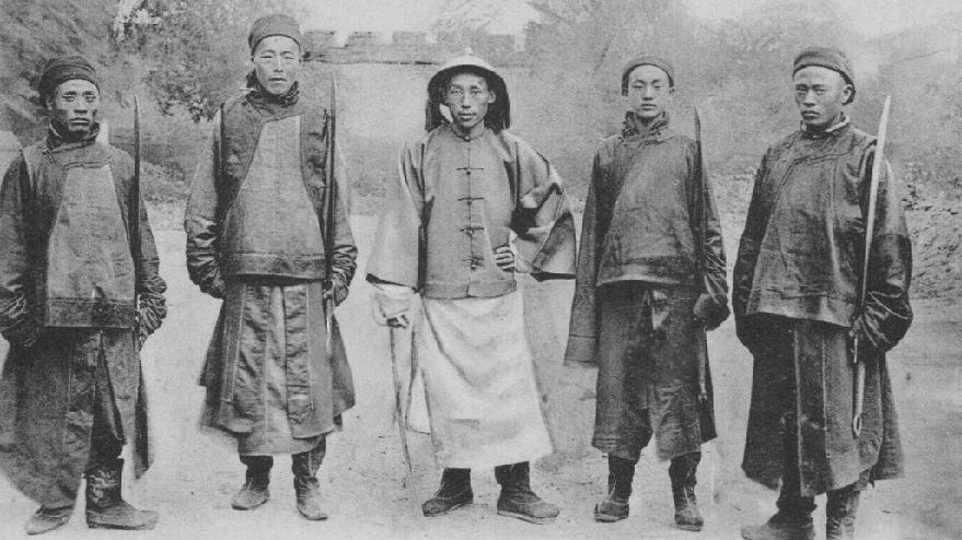 这张照片拍摄于清末，五个男子身着传统的清代衣服，手里都拿着刀，整体风貌带有鲜明的