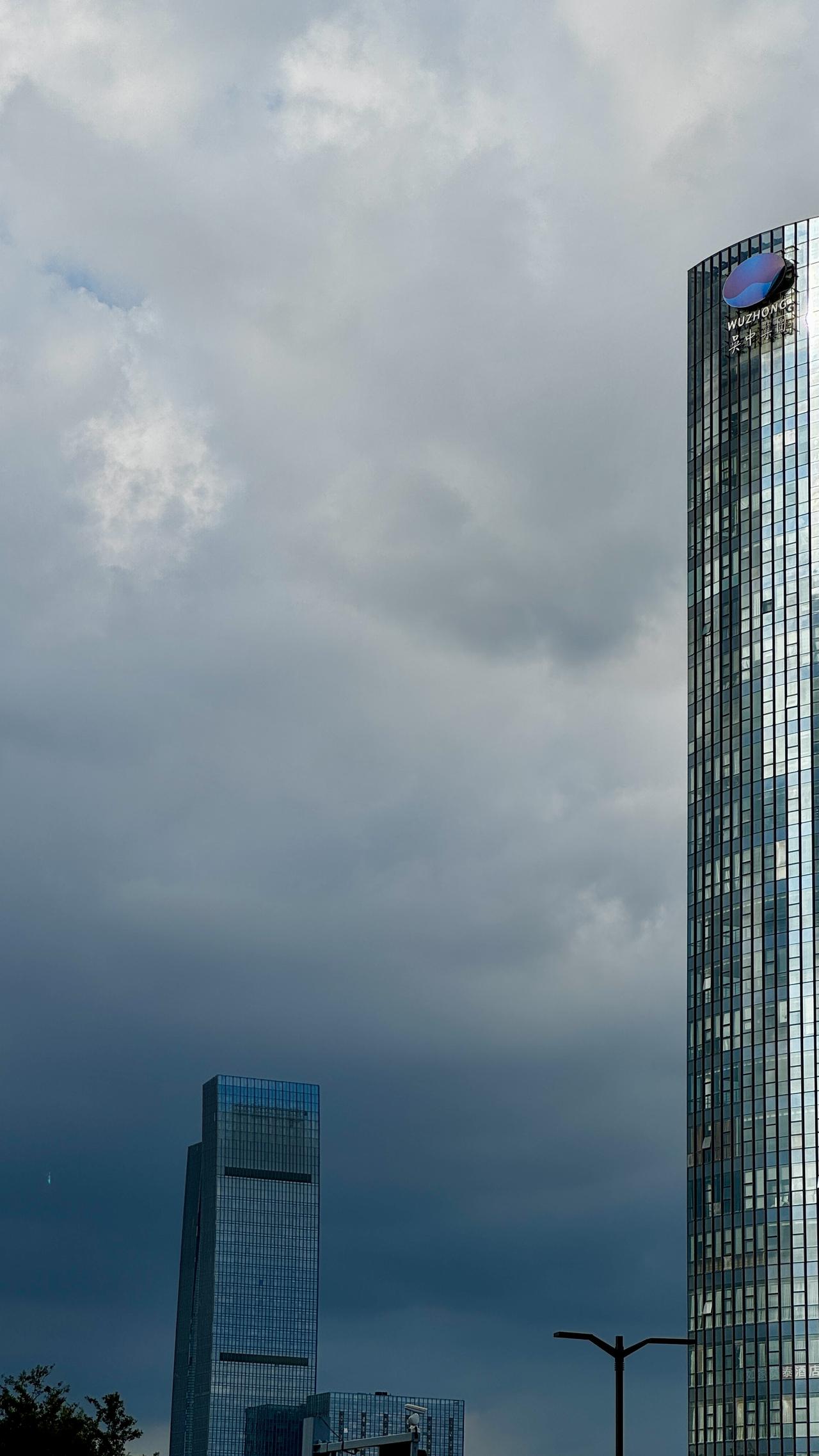 街拍城市建筑厚重云层笼罩城市，玻璃楼宇刺破天际，喧嚣暂隐，只剩建筑与风云无声对望