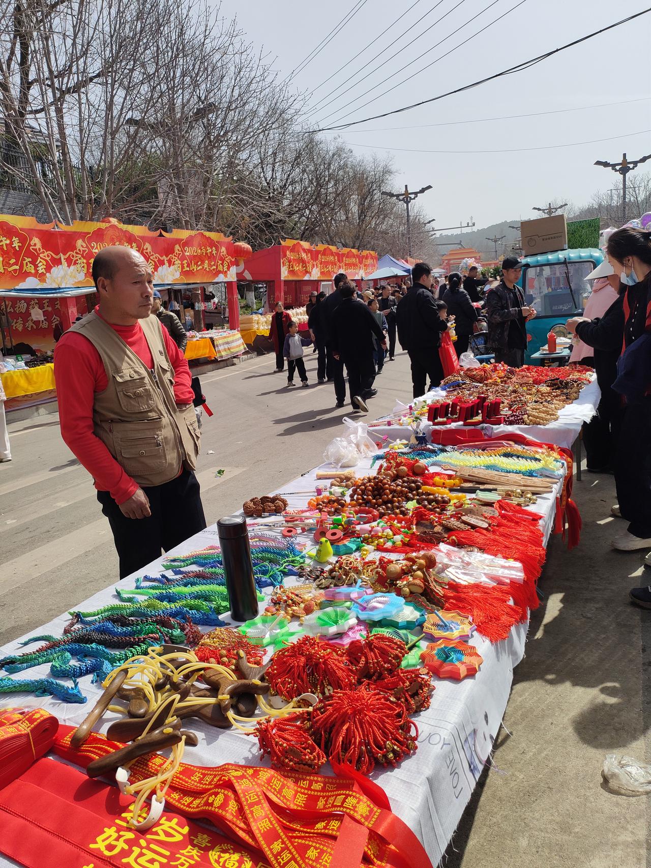 春日生活打卡季红绸飘带、木珠手串，集市的摊位上摆满了带着烟火气的小物件，人潮涌动