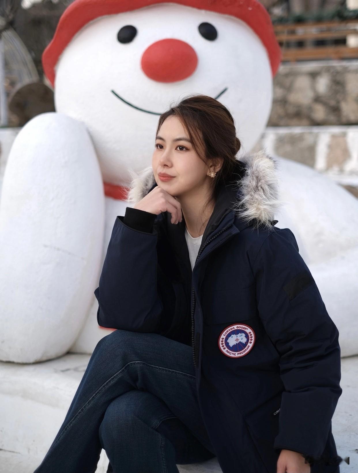 紧身牛仔裤配什么颜色的上衣好看穿着深蓝色厚羽绒服搭牛仔裤，站在圣诞树旁。