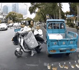车水马龙的马路上，一个妈妈骑着电动车，带着三个女孩正要过马路，一辆电动三轮车贴着