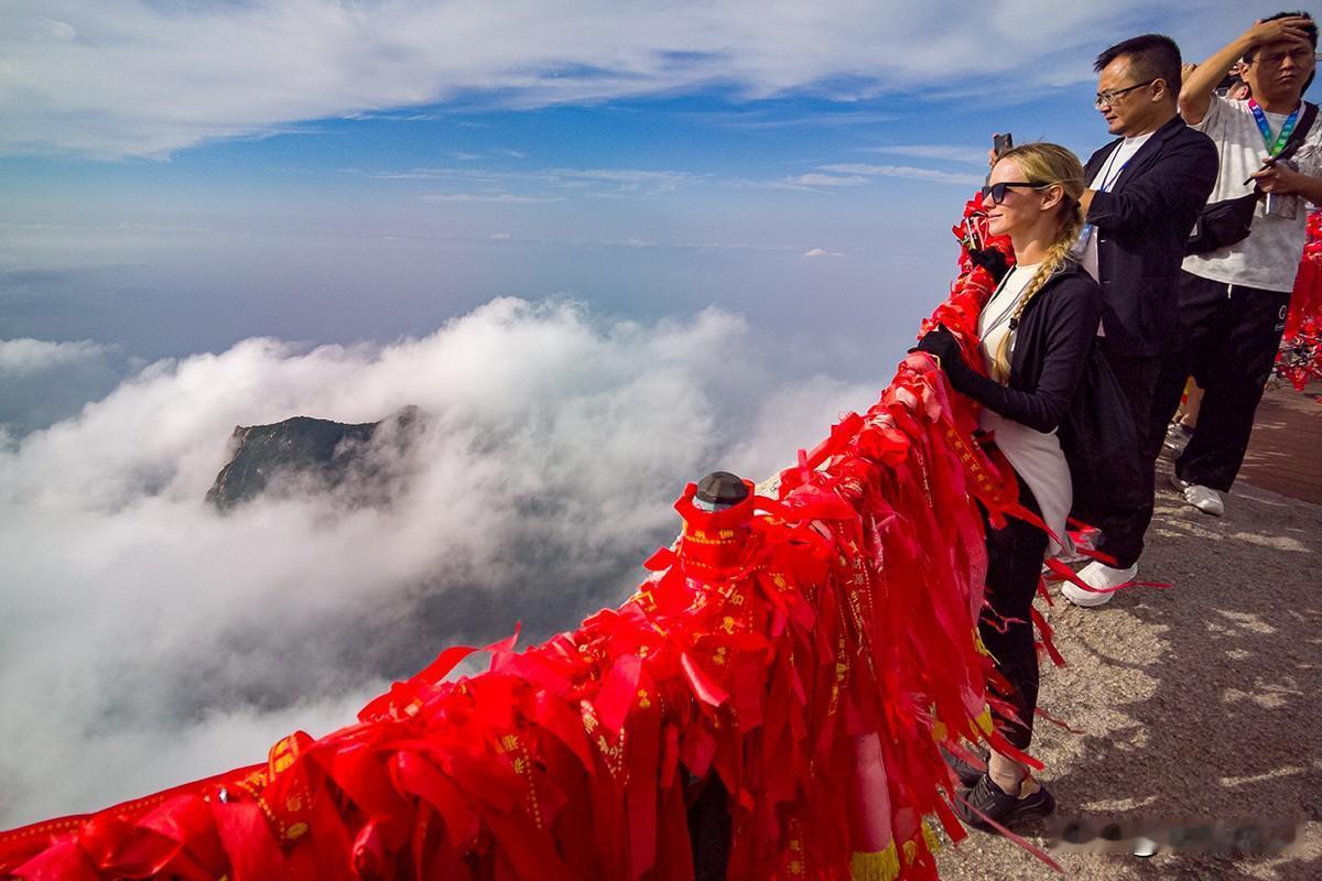 西峰金发女拍云海
       华山西峰之巅，云海翻涌如仙境，蓝天白云下红绸祈愿