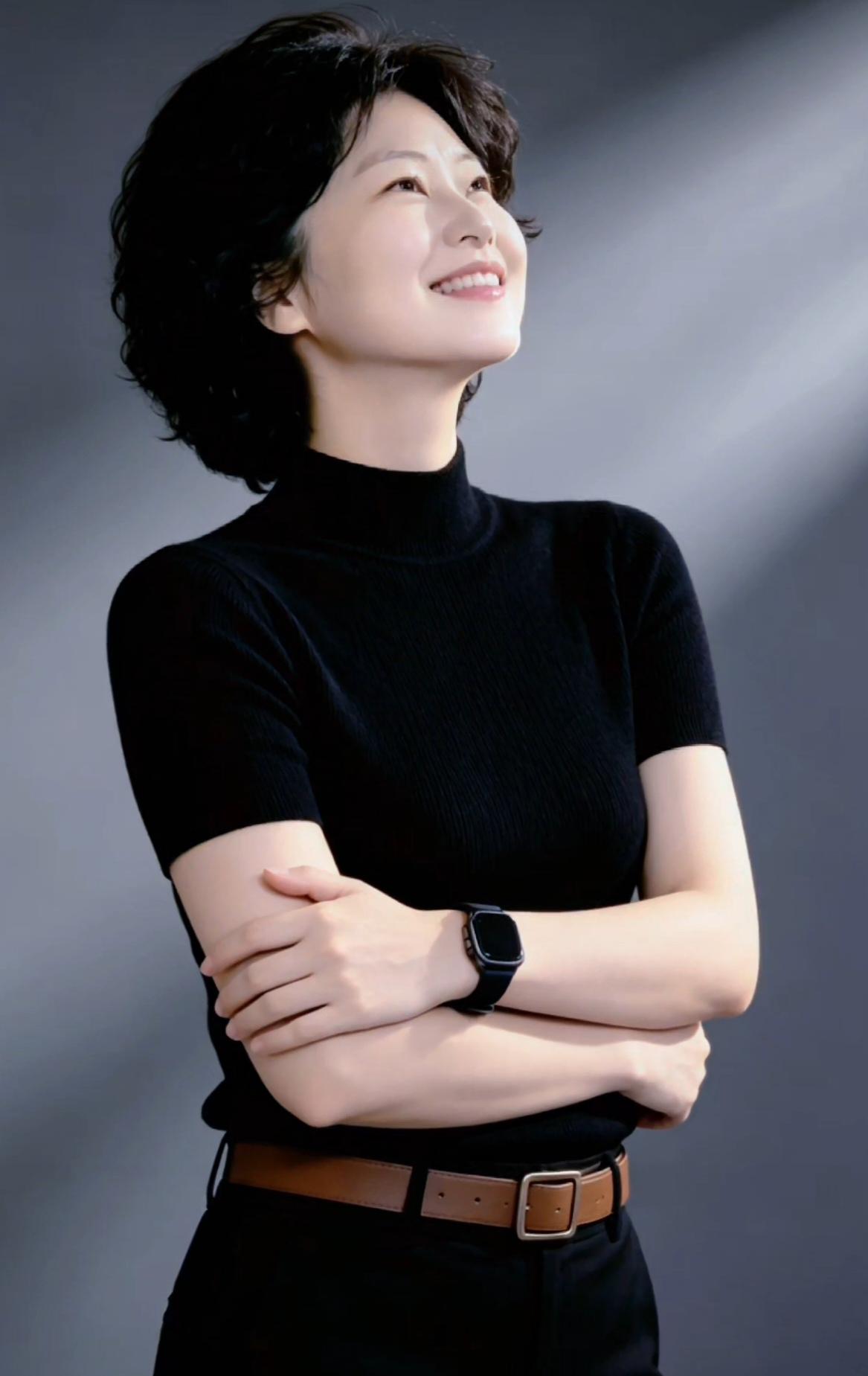 这位女士微笑着看向远方，双手交叉。