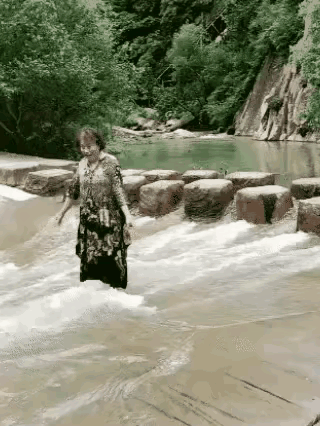这位大妈在景区闲逛时，被小型水库的景色吸引，径直走到水库下游临水区域打卡拍照，还