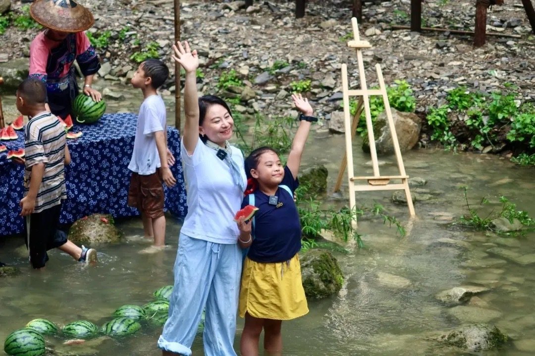 矮寨的夏天能有多快乐 苗家阿妹把西瓜泡在溪水里，游客围坐四方桌把脚浸在凉水中，德