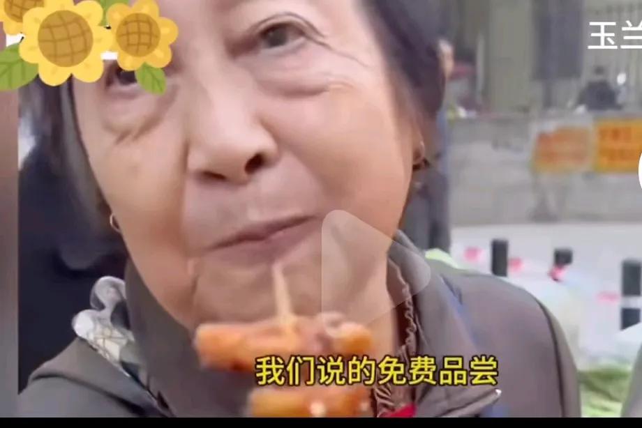路边有卖炸货的说是免费品尝这老太太快吃饱了。这老太太站在边上边吃边拿，商家提醒她