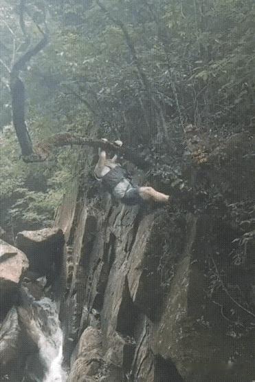 老哥在一处野外踏青，双手抱住崖壁上的一棵树作出不少惊险动作，让人看着是心惊胆寒。