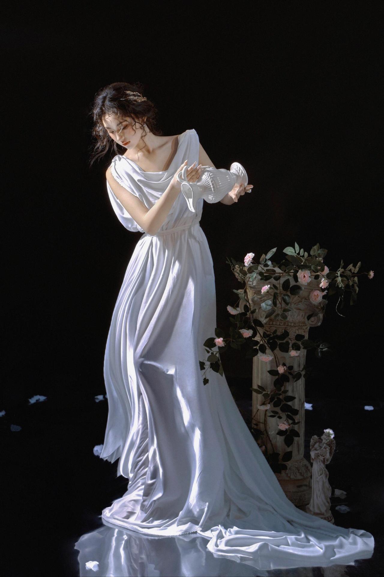 当黑色背景如幕布般拉开，白色百合似月光碎屑在画面绽放，身着素白长裙的女子轻捧金色