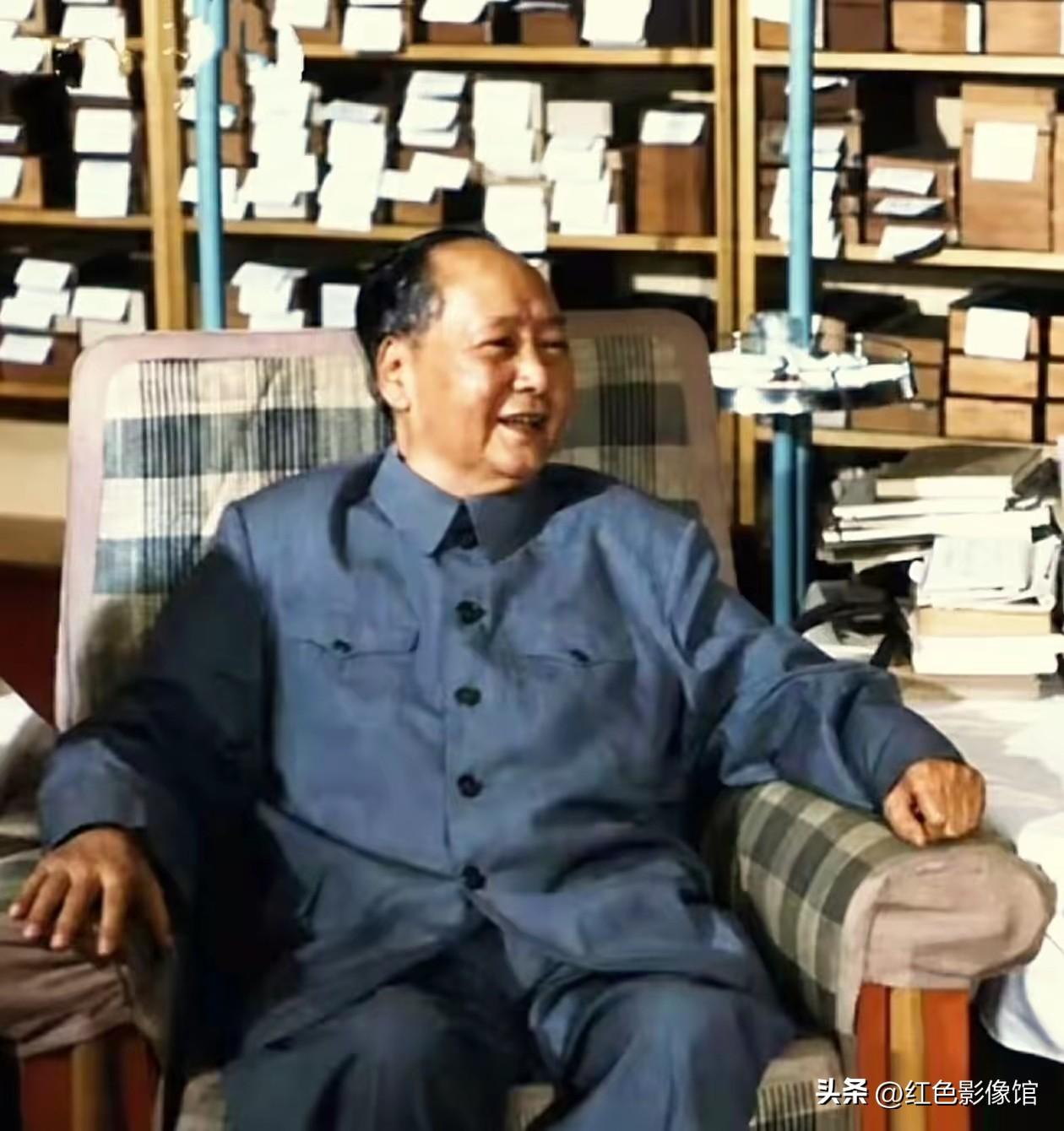 毛主席身着深蓝色中山装，坐在格子布艺扶手椅上，神情舒展、面带笑意；背景书架堆满书