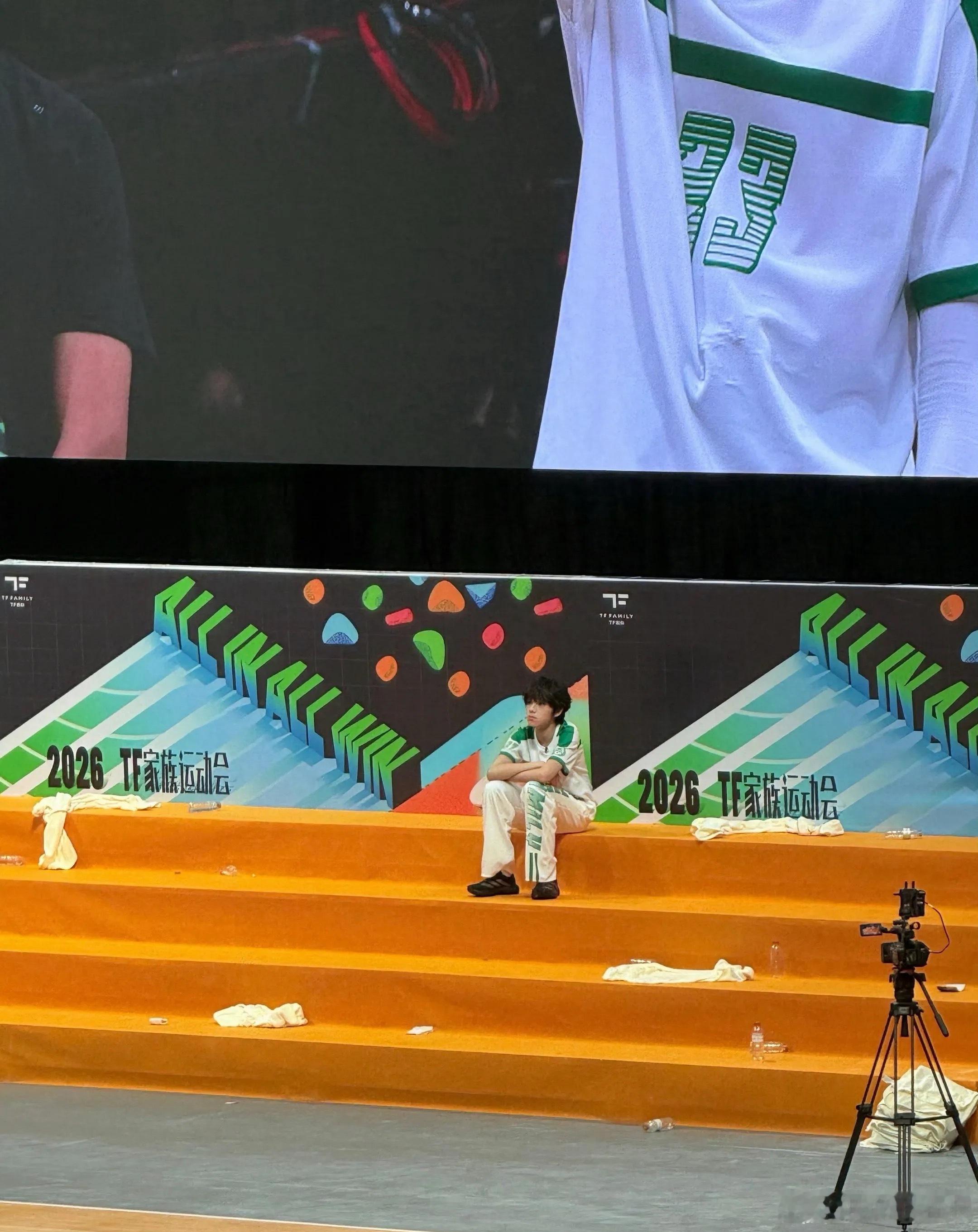 王橹杰运动会一个人坐着身边伙伴结伴走动观赛，欢声笑语环绕四周，王橹杰独自静坐放空