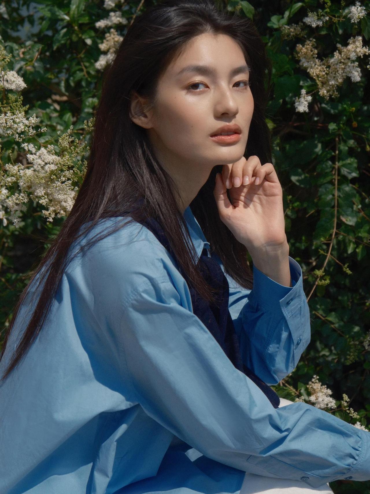 这组春日漫步少女人像，,画面以大面积自然绿为基底，搭配浅蓝衬衫与白色半裙，色彩上