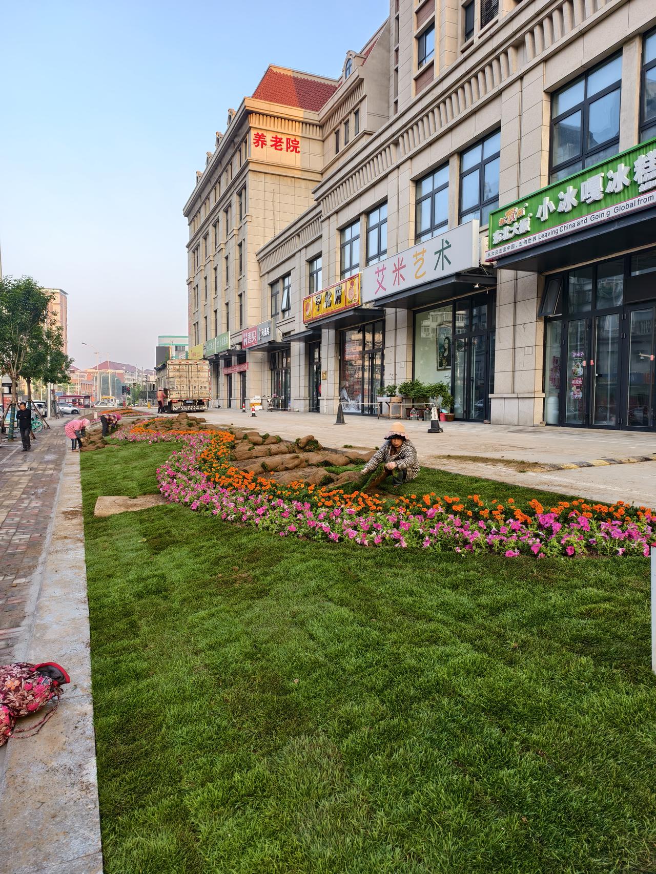 南开区西营门外大街与临汾路交口又一处景观绿地正在铺设中，漂亮的绿草鲜花点缀着城市