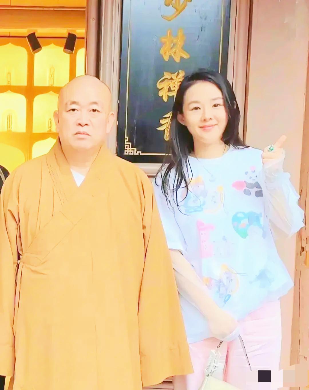 瞅瞅这张释永信的合影，
大和尚的脸板得比城墙还硬，身旁的女士却笑开了花，这画面反