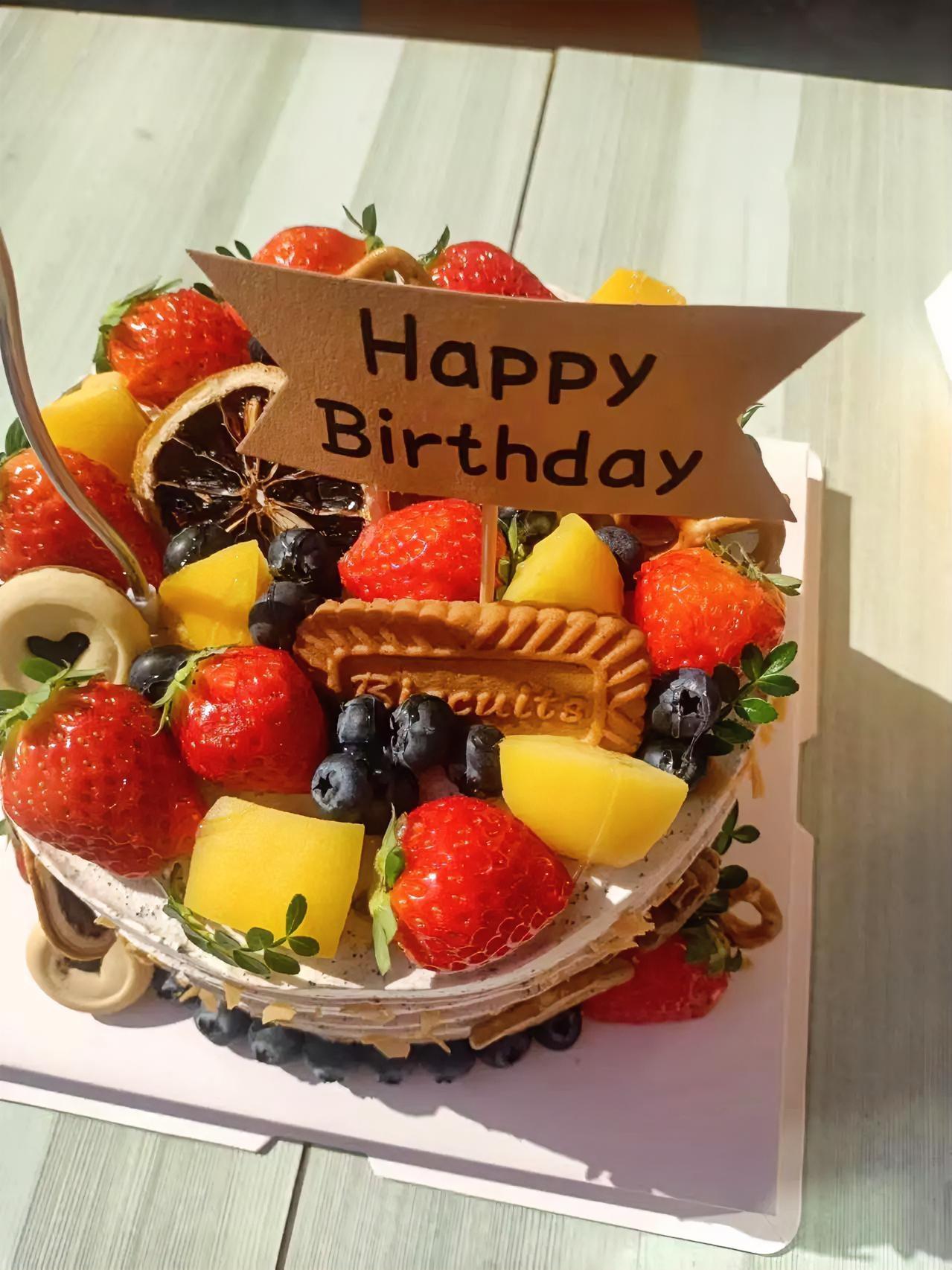 这只生日蛋糕像一份被精心包裹的祝福，新鲜的草莓、蓝莓与黄桃在奶油上铺开，饼干与干