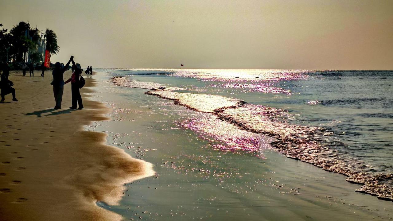 分享一张最近随手拍的照片落日把碎金泼在浪尖，沙滩的脚印裹着咸风。那只举高的手，是