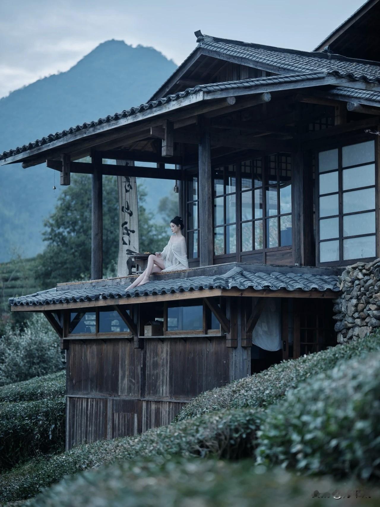 黛瓦层檐覆野烟，木窗云影共缠绵。
佳人静倚危栏畔，素袂轻垂晚风前。
翠岭含苍凝远