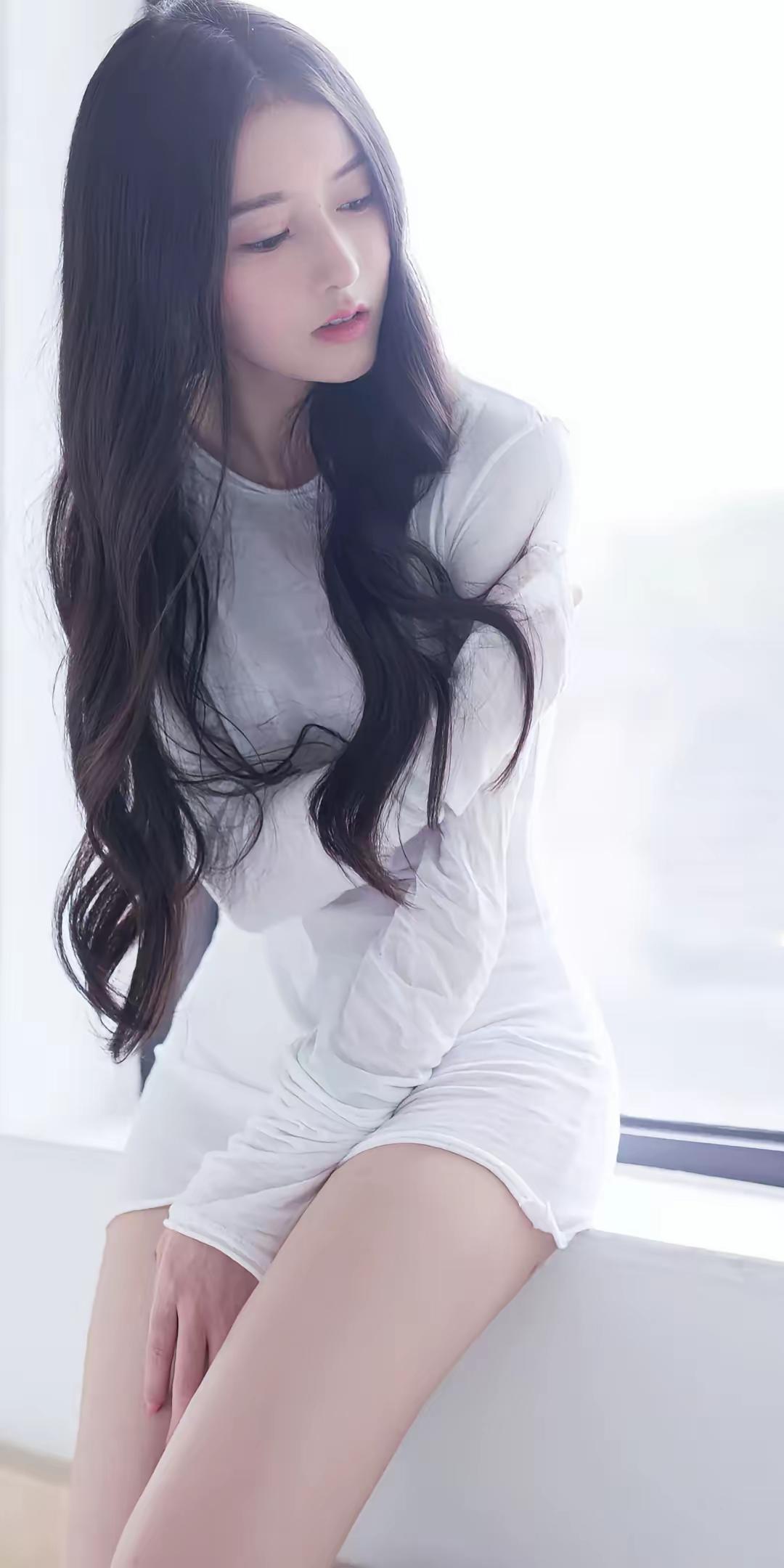 长发美女坐在窗边，穿白色连衣裙。