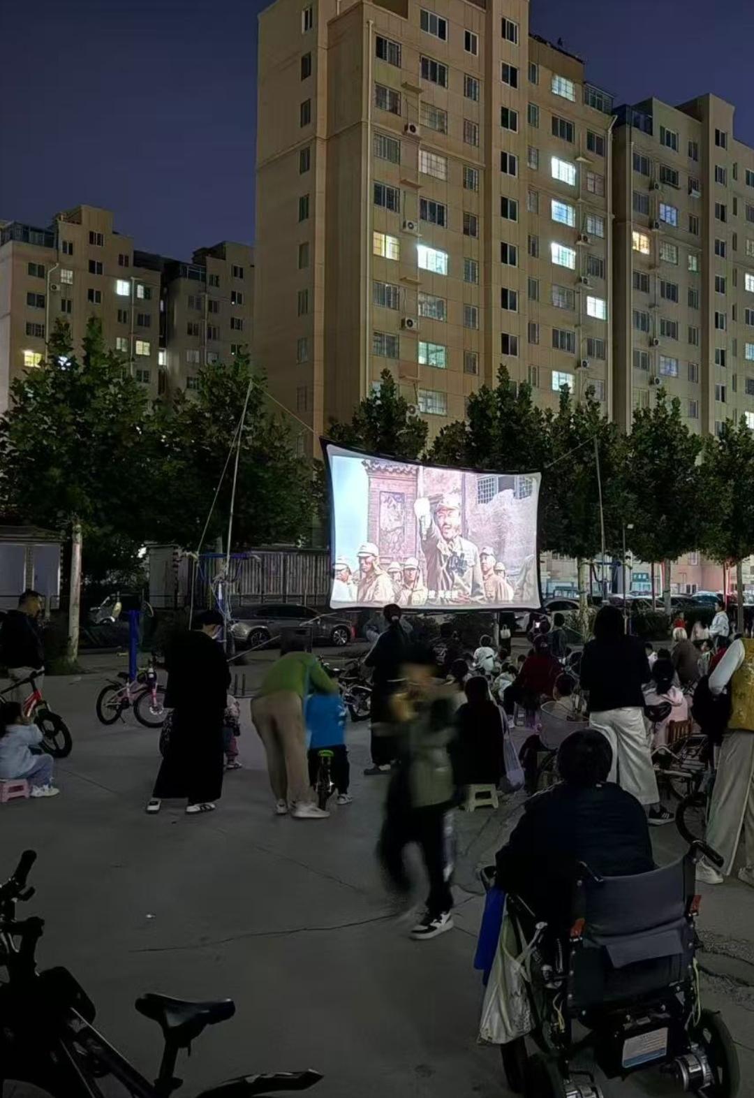 小区广场上放电影🎦，大家坐着看热闹。这样的场景不多了吧。放的电影是举起手来✋?
