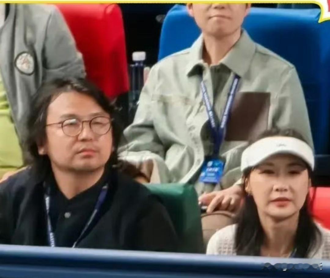 雷佳音和老婆现身上海劳力士大师赛看球，穿着黑色西装，戴着眼镜，留着一头长卷发，蓄