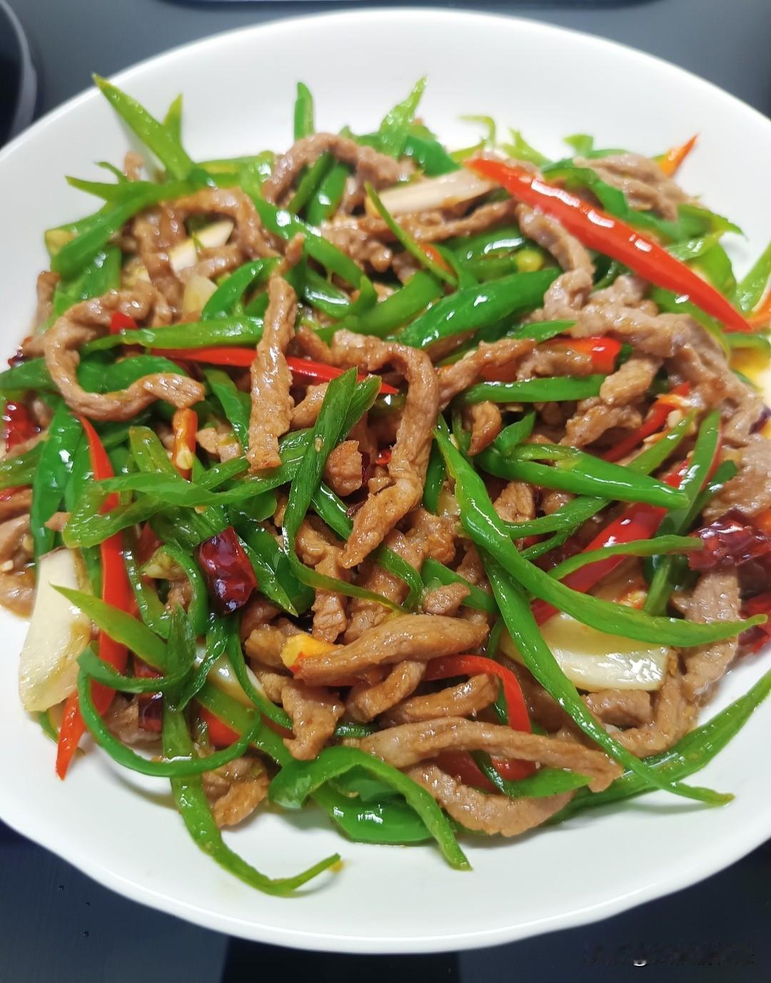 母亲挑选鲜嫩薄皮青椒，去籽切细条，瘦肉顺纹切丝，少许生抽淀粉抓匀腌渍，肉质软嫩不