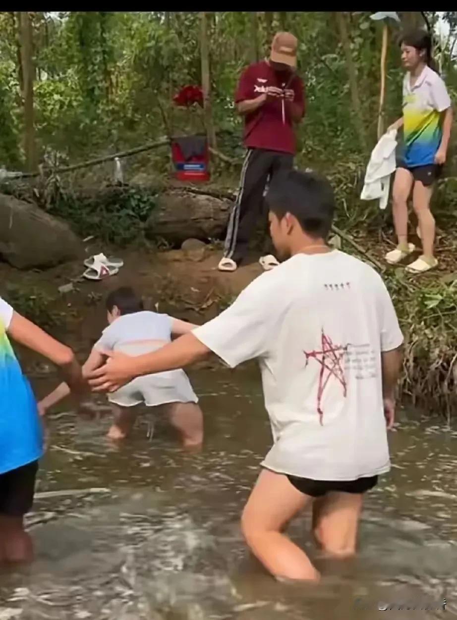全红婵与同村小伙伴下塘摸鱼，全然不顾自己的冠军身份。很好奇，岸上站着的那件“红卫