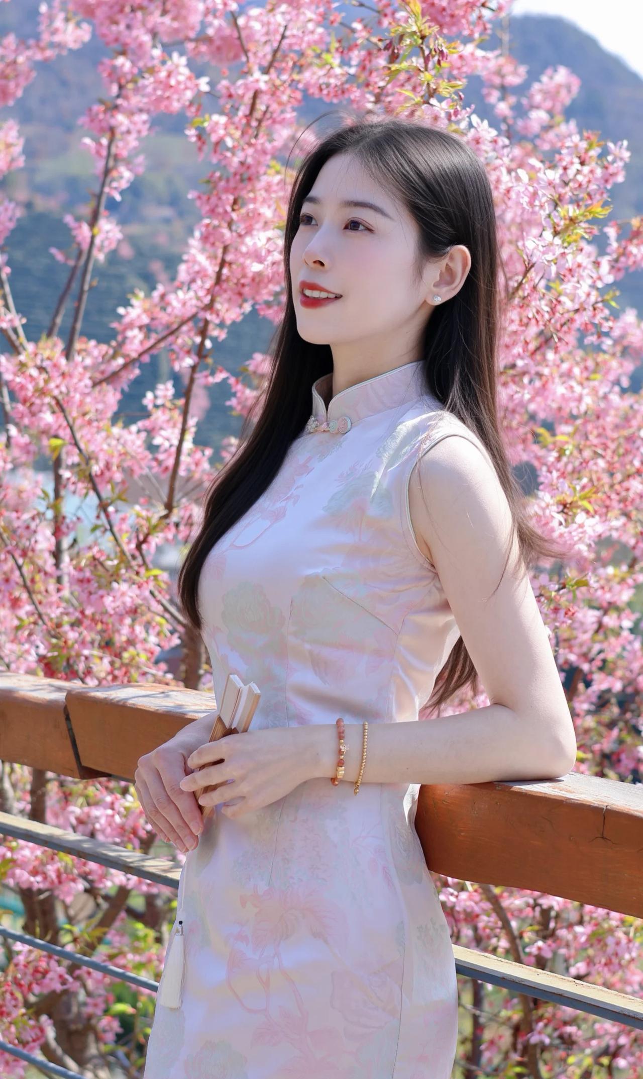 👘 穿搭与造型
少女身着淡粉底色无袖旗袍，裙身绣着浅绿与柔粉的花卉暗纹，领口缀