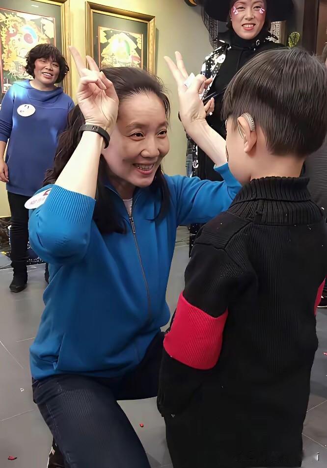 退休之后的李修平留起了长发，她在美术展馆里有小朋友跟她一起互动留影，她蹲下身跟小