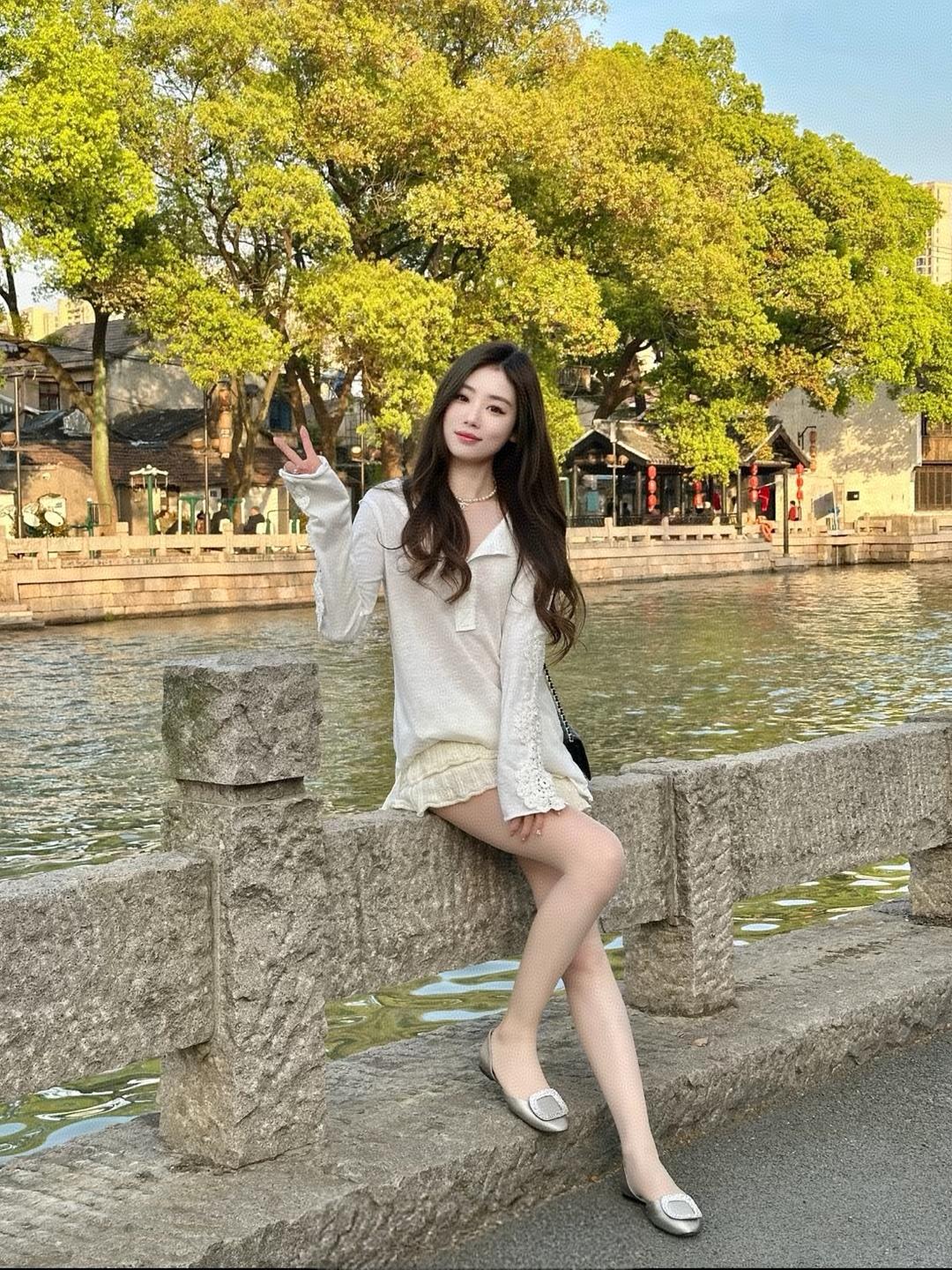 阳光明媚的午后，少女在河畔轻倚栏杆，微笑着比出V字手势，享受着悠闲时光。
