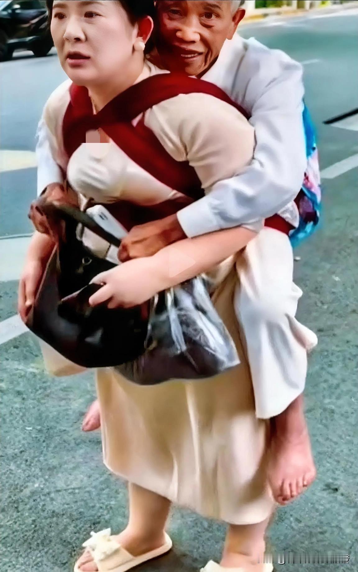 女子用背带托着老人，把他整个人驮在后背上，老人则双手在前提着袋子和包，女子同时也