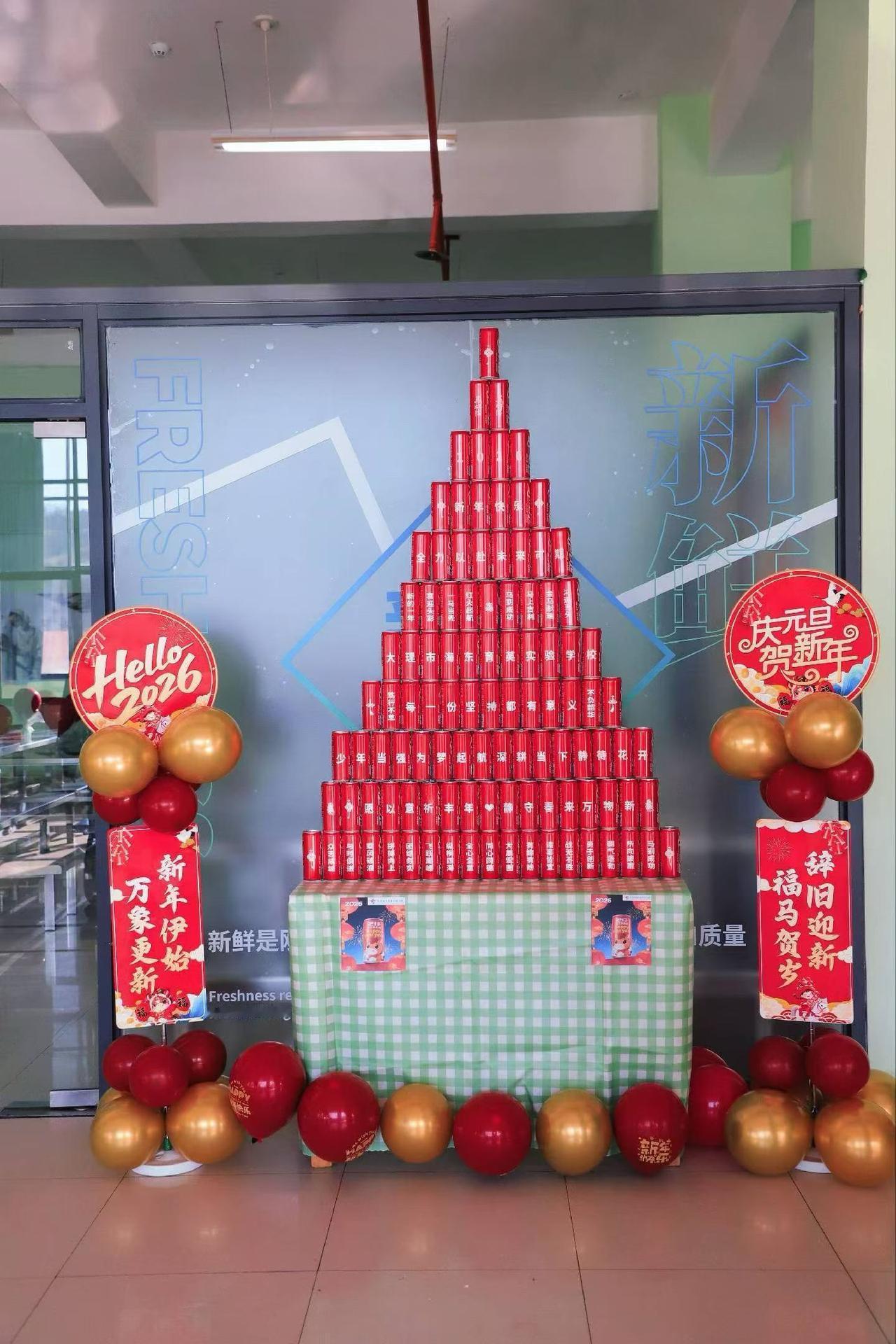 学校这新年布置可真喜庆！

桌上红通通的易拉罐搭成小金字塔，在绿格子桌布上特别显