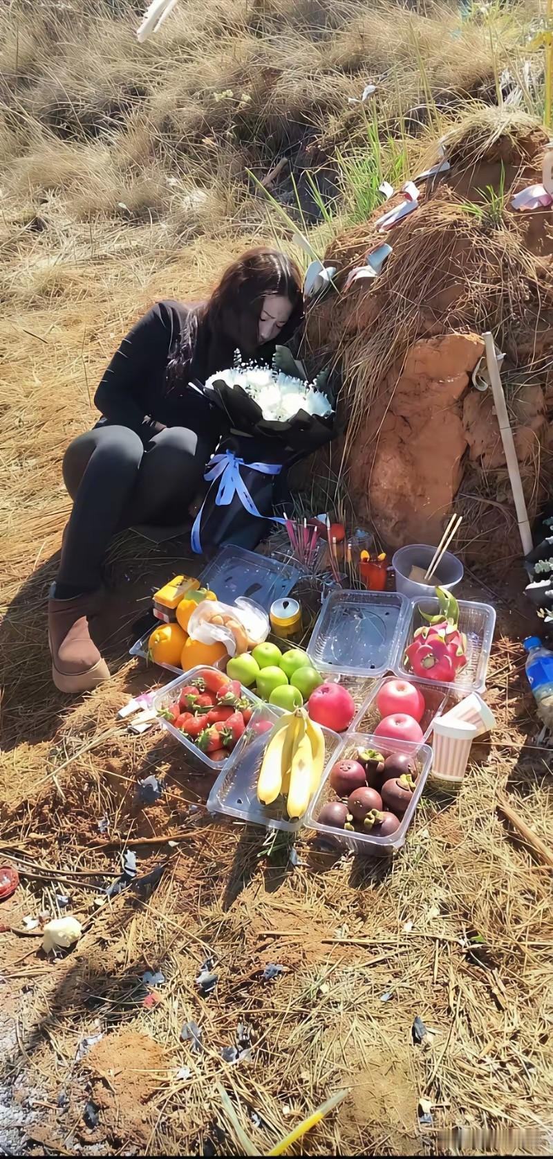 女子倚在一座坟前，坟前摆放着各种水果，她手里捧着一束花，感觉非常的伤感，非常的难
